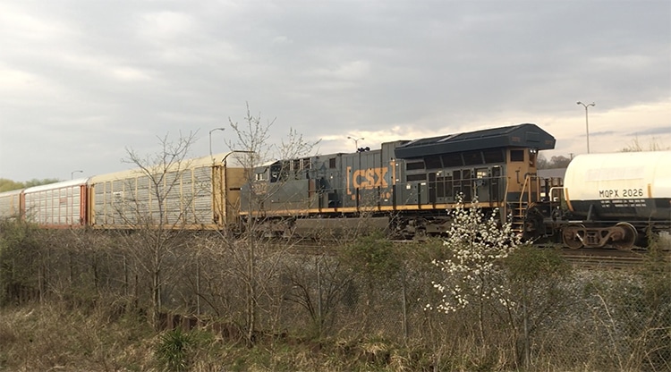 A CSX locomotive operated by a two-person crew powers a train with a mix of freight and tanker cars.